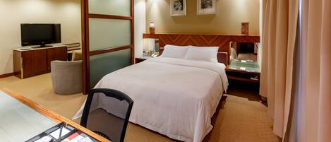 A hotel room with a large bed, a desk with a computer, a television, and a small table with a lamp.