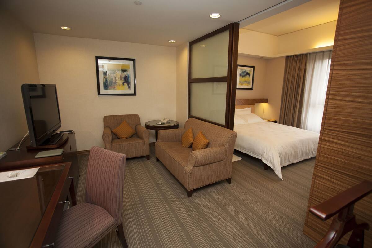 Habitación de hotel con cama, sofá, silla, escritorio con televisor y una mesita.