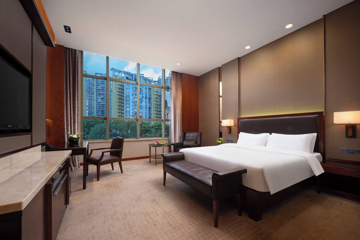 Habitación de hotel con una cama grande, un escritorio, una silla, un televisor y una ventana con vistas a la ciudad.