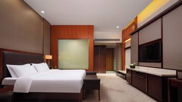 A modern hotel room with a large bed, a flat-screen TV, a desk, and a seating area.