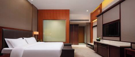 A modern hotel room with a large bed, a flat-screen TV, a desk, and a seating area.