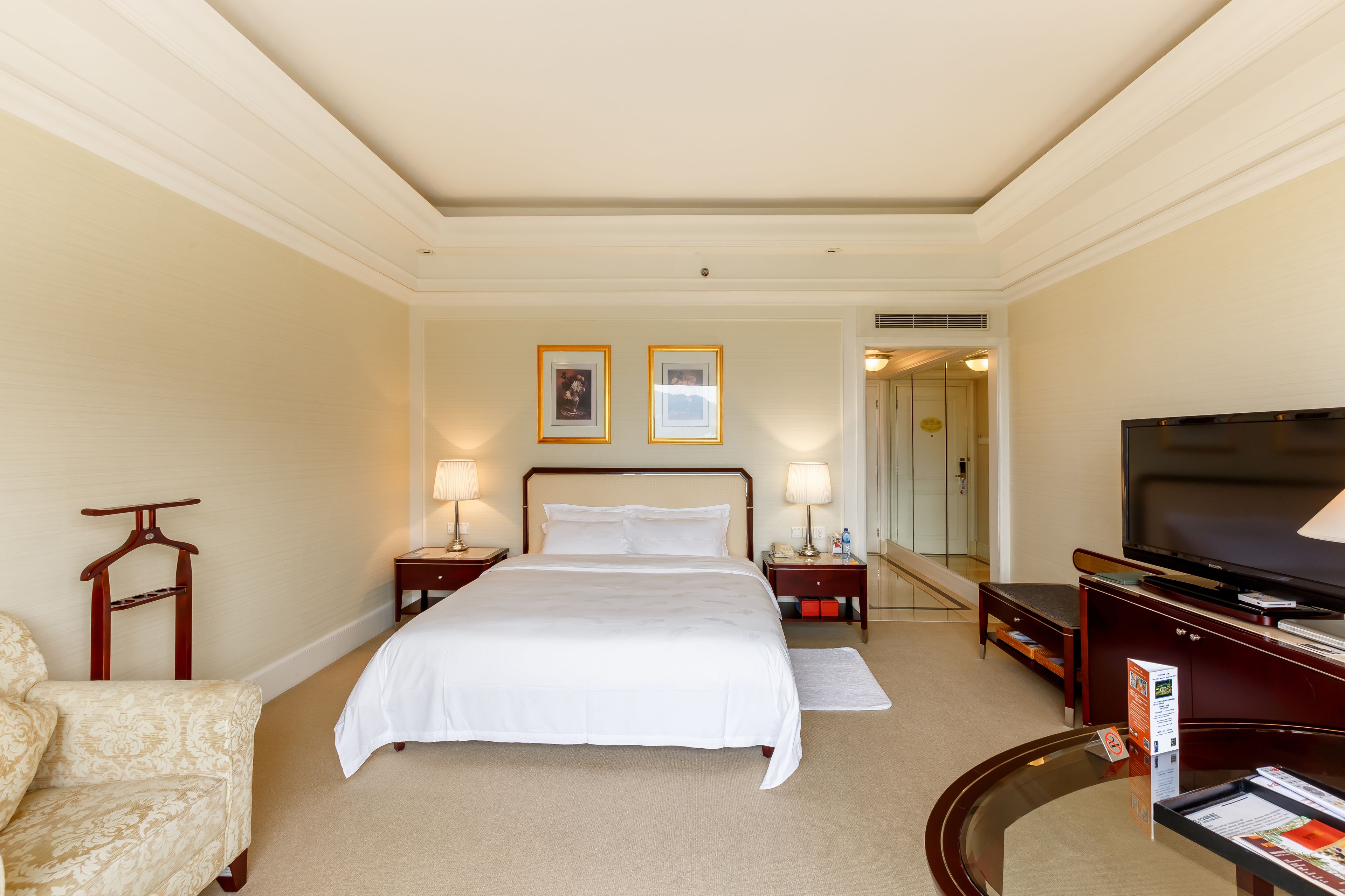A hotel room with a large bed, two bedside tables with lamps, a TV, a wooden chair, and a mirror.