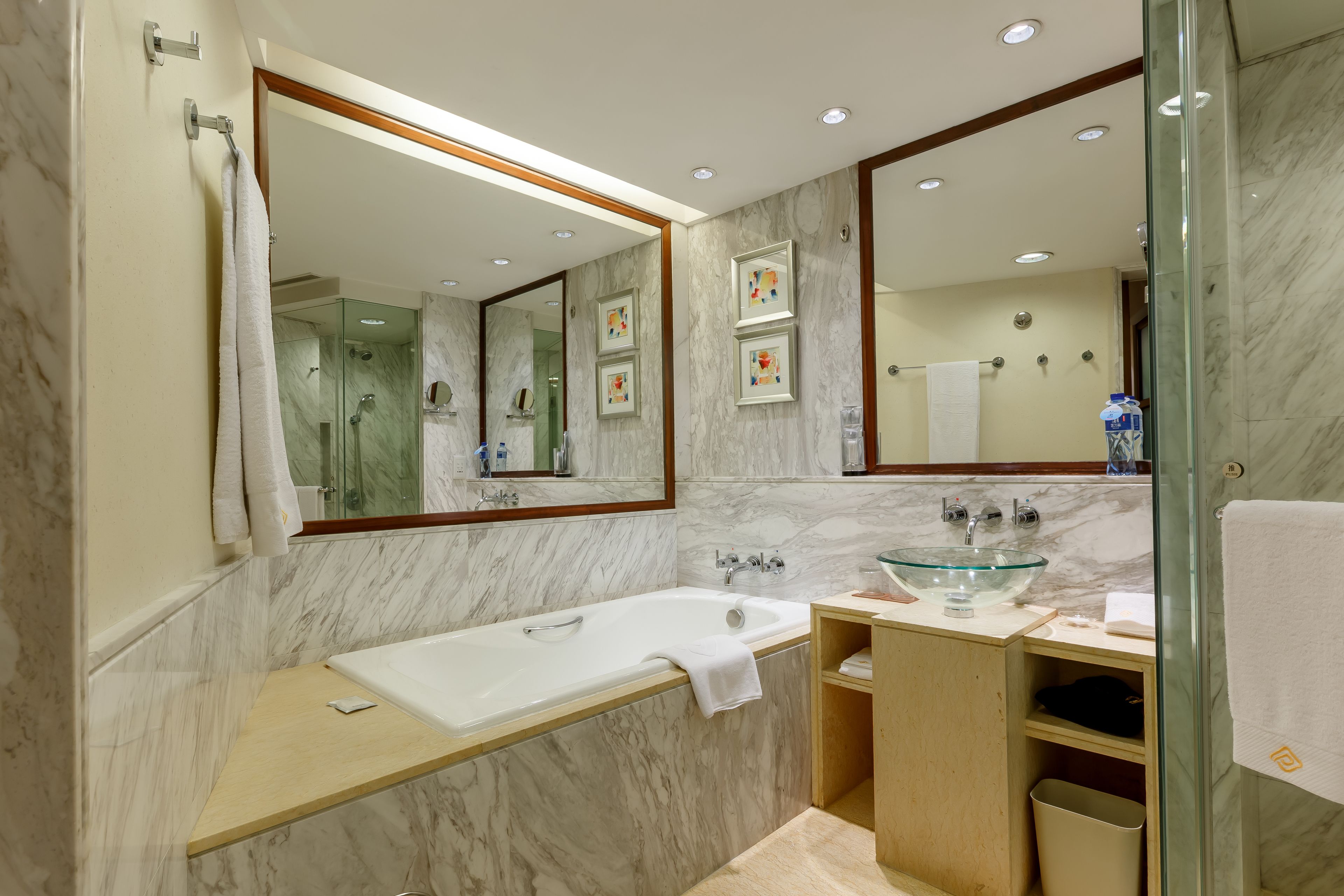 A modern bathroom with a marble wall, a glass sink, a large mirror, and a shower area.