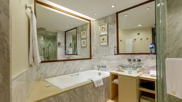 A modern bathroom with a marble wall, a glass sink, a large mirror, and a shower area.