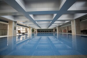 Una piscina interior con agua azul cristalina, suelo de baldosas y techo con diseños geométricos.