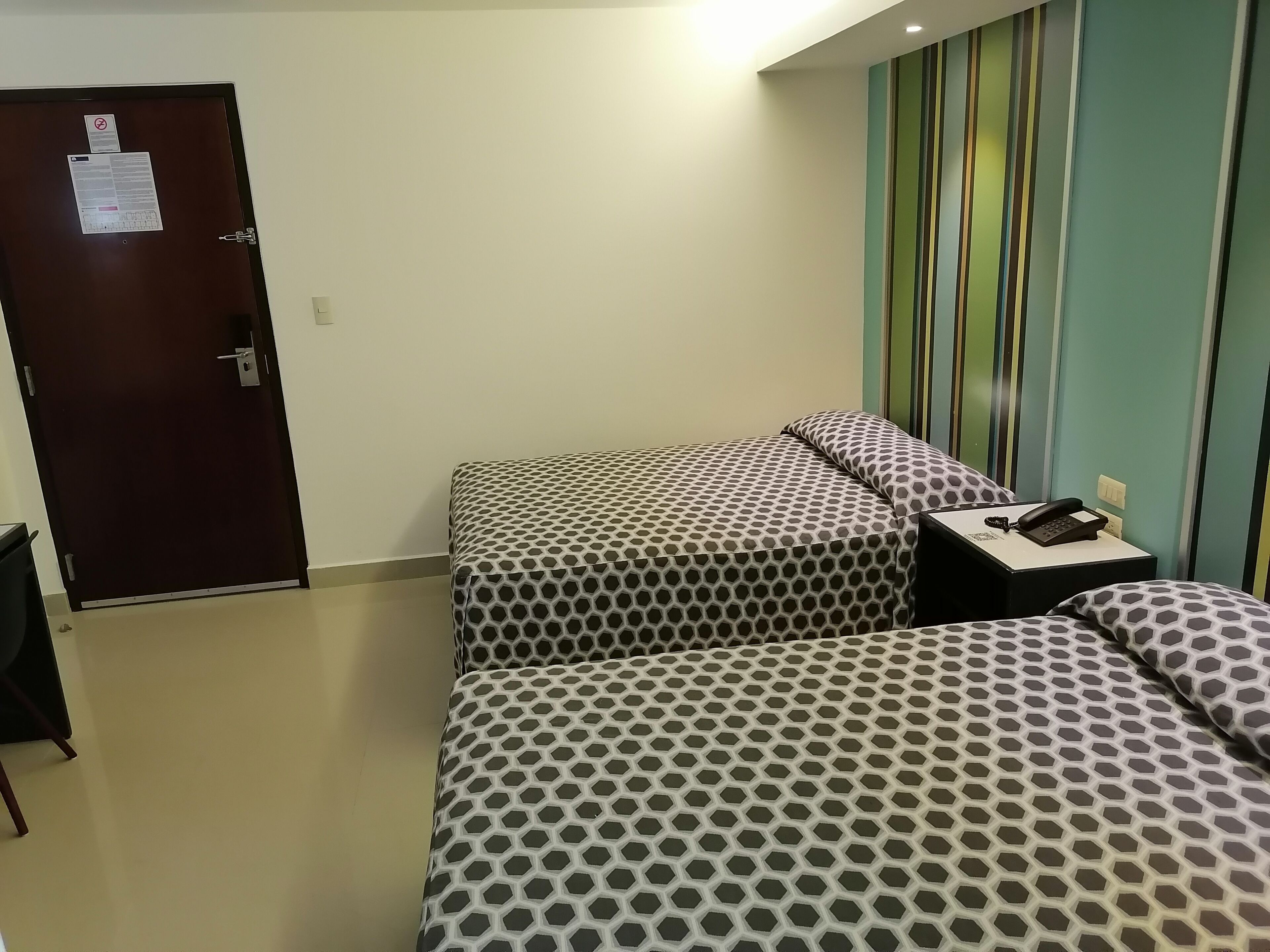 Habitación de hotel con dos camas, un escritorio con teléfono y una puerta con un aviso.