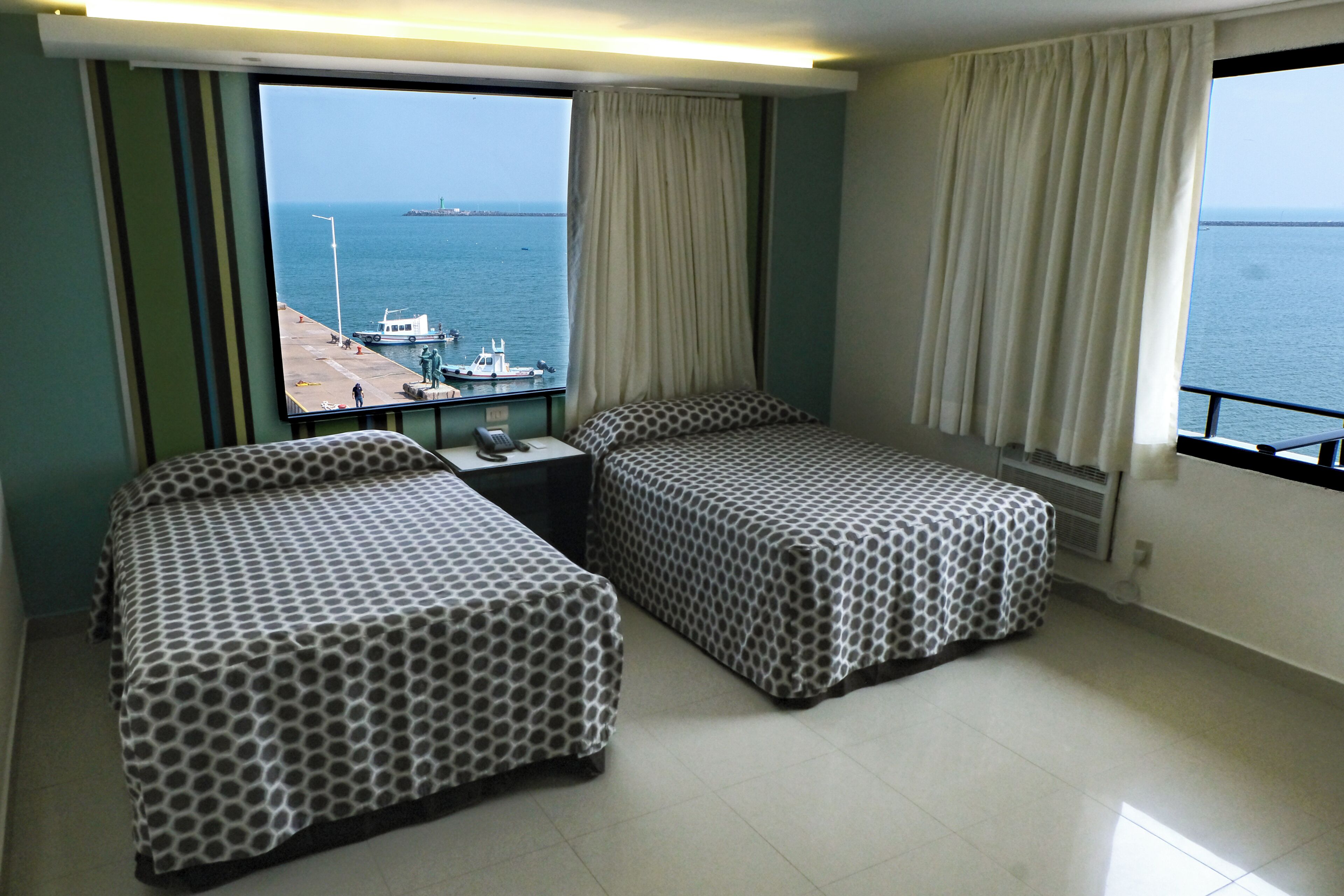 A hotel room with two beds, a small table, and a view of the sea and boats.