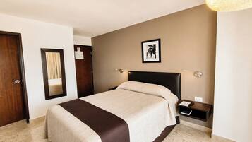 A hotel room with a bed, a nightstand, a wall-mounted lamp, and a framed picture.
