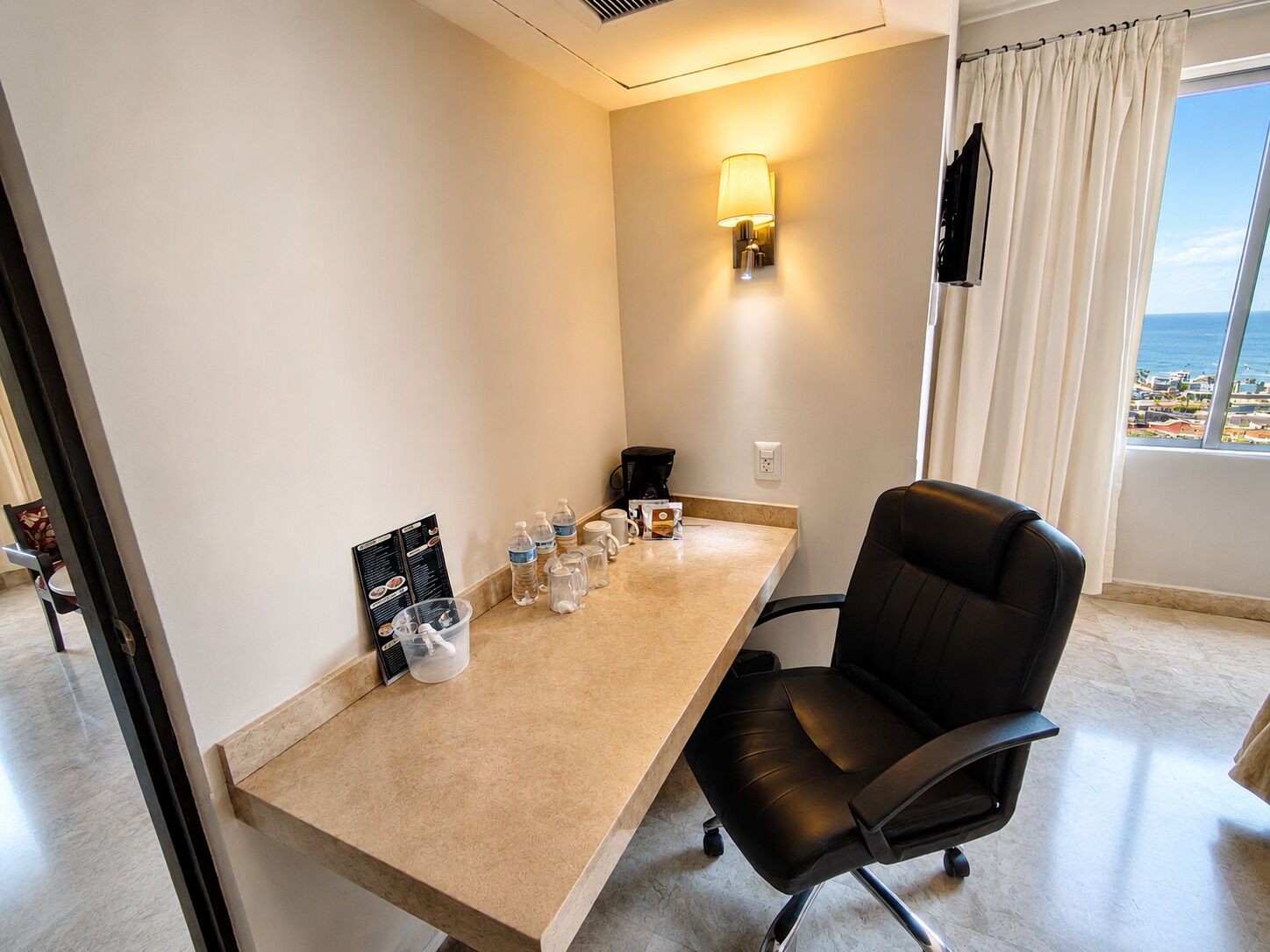 A hotel room with a desk, chair, and a view of the sea.