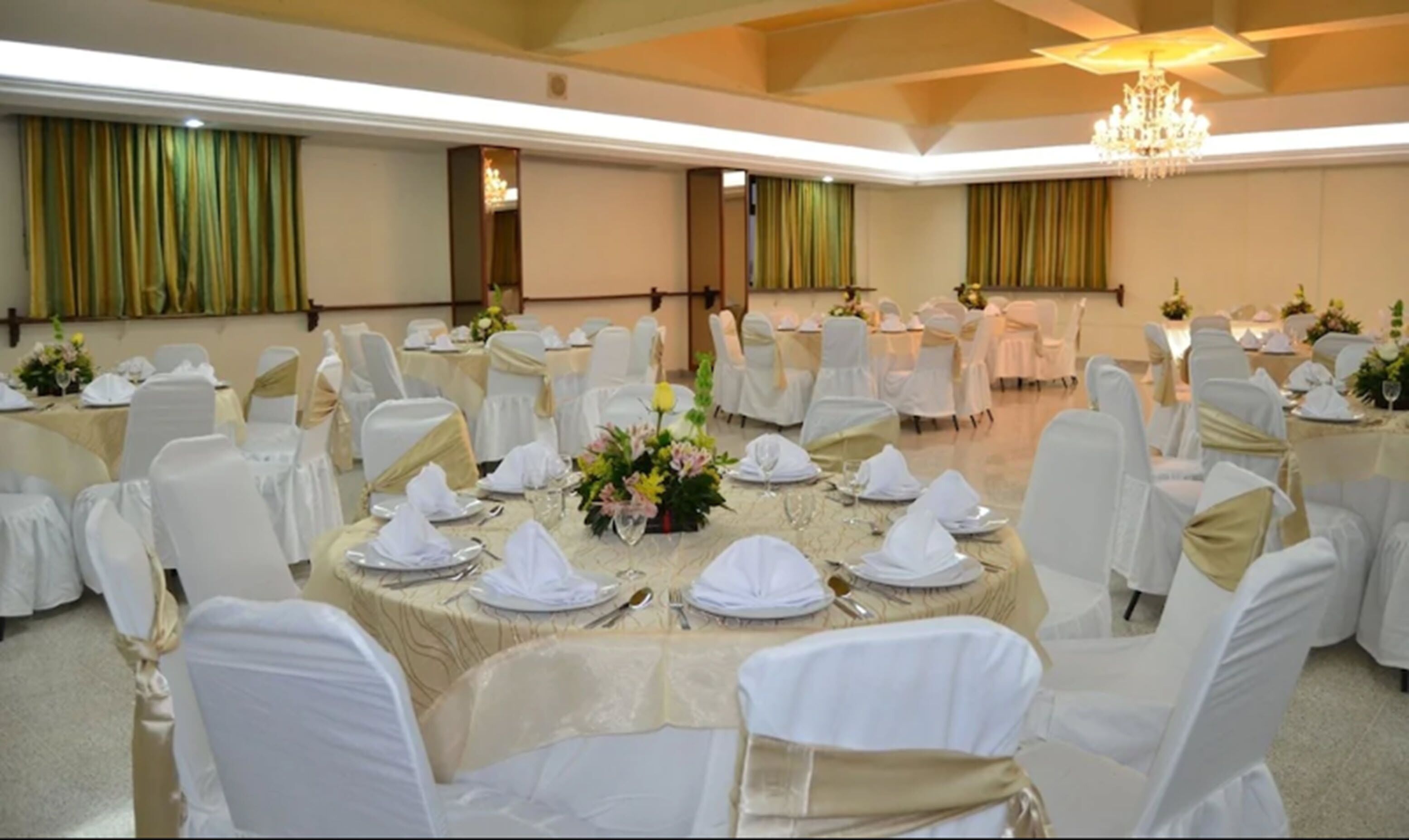 Un salón de banquetes con mesas redondas dispuestas para cenar, sillas blancas y candelabros.