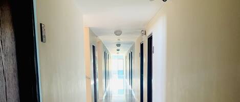 A long, well-lit hallway with doors on both sides, leading to rooms.