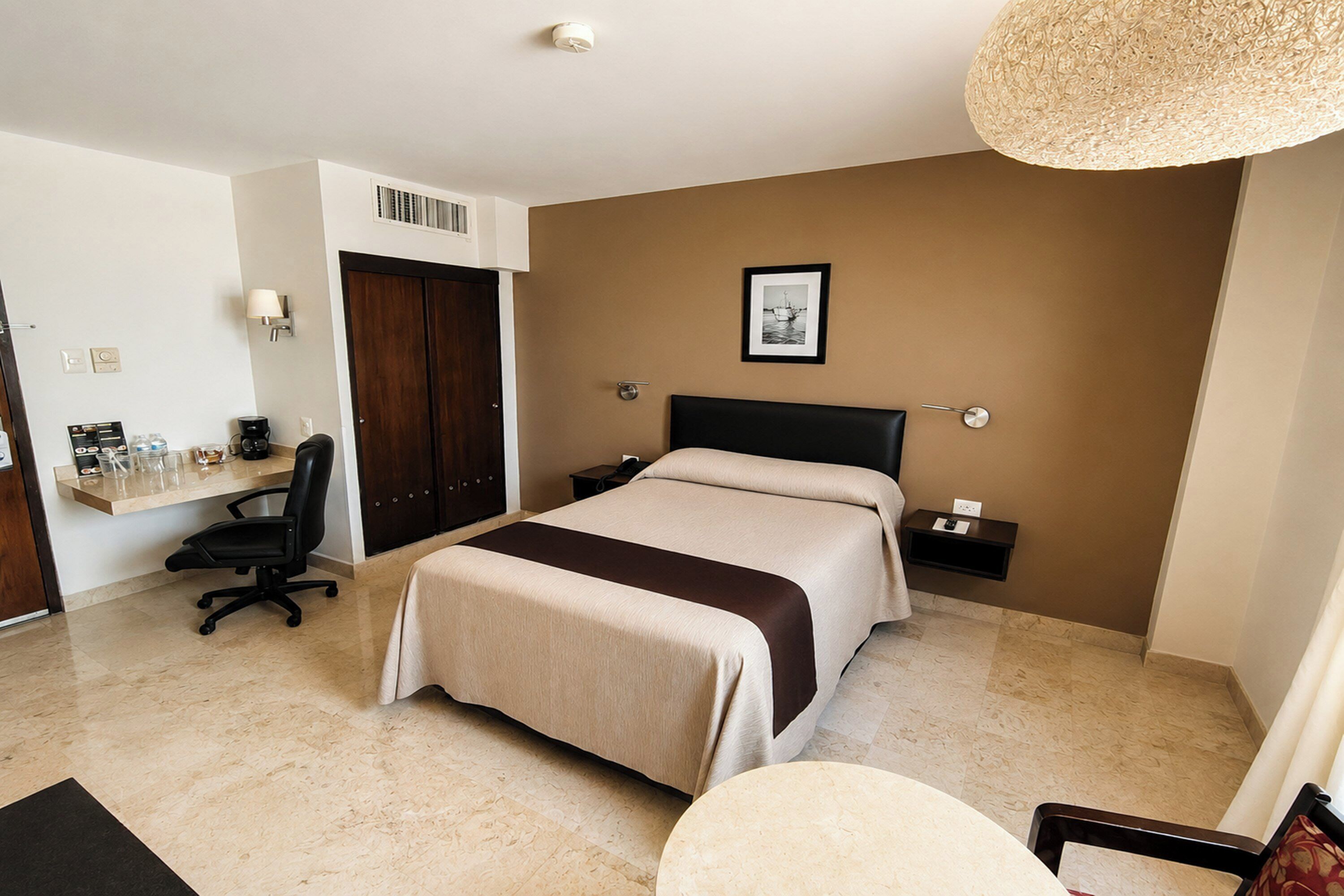 A hotel room with a bed, desk, chair, bedside tables, and a picture on the wall.