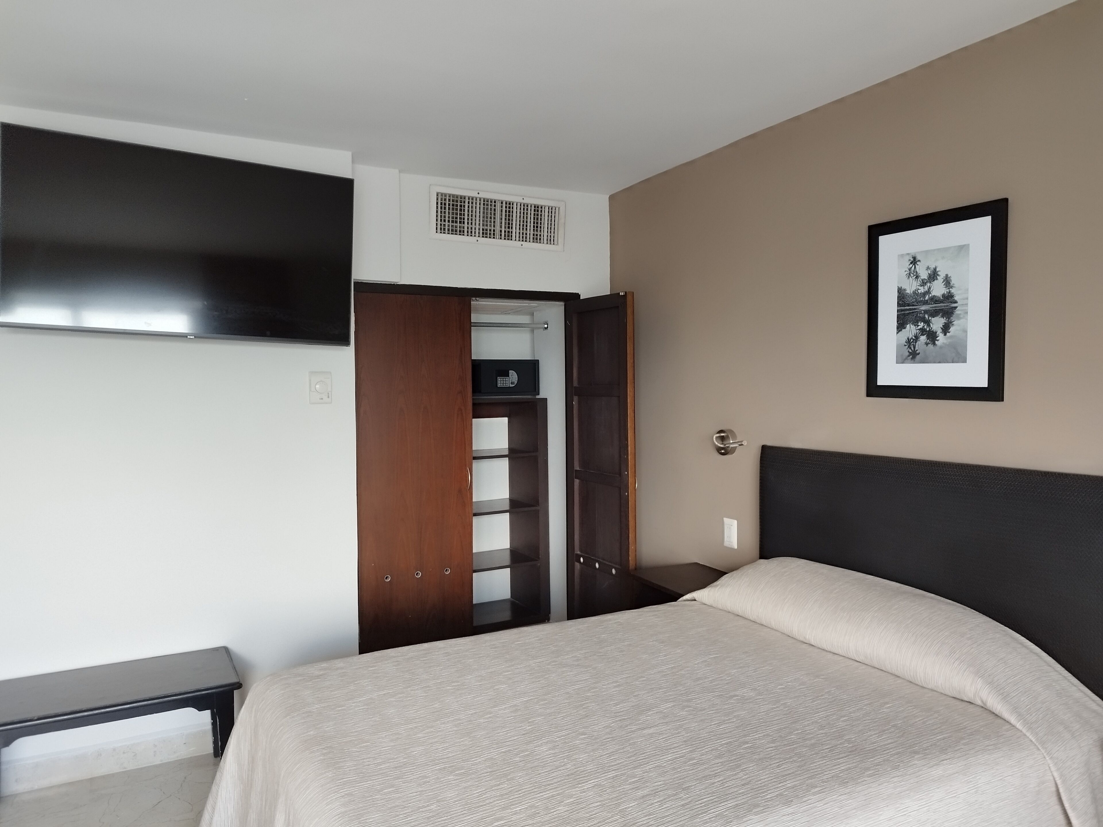 A hotel room with a bed, a wardrobe, a desk, and a TV mounted on the wall.