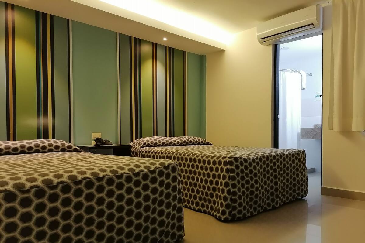 A hotel room with two beds, striped wallpaper, a nightstand, and an air conditioning unit.