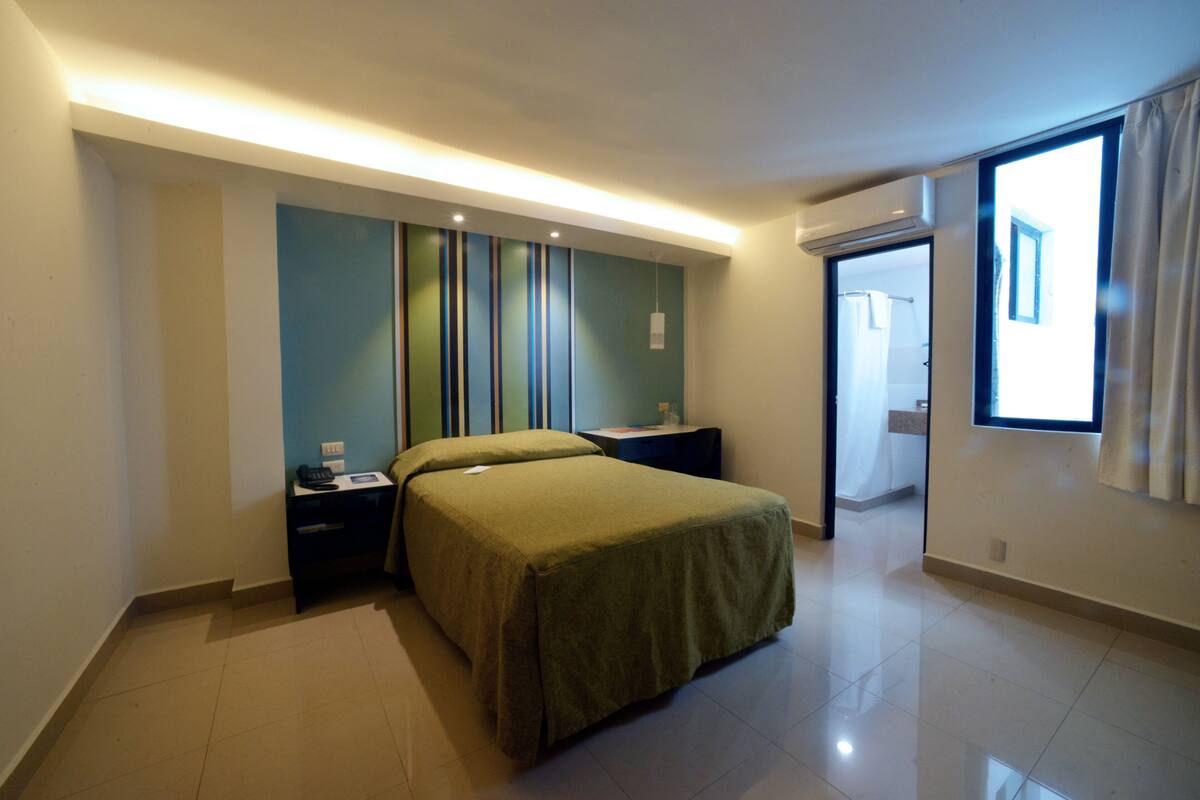 A modern hotel room with a large bed, bedside tables, a mirror, and a window.