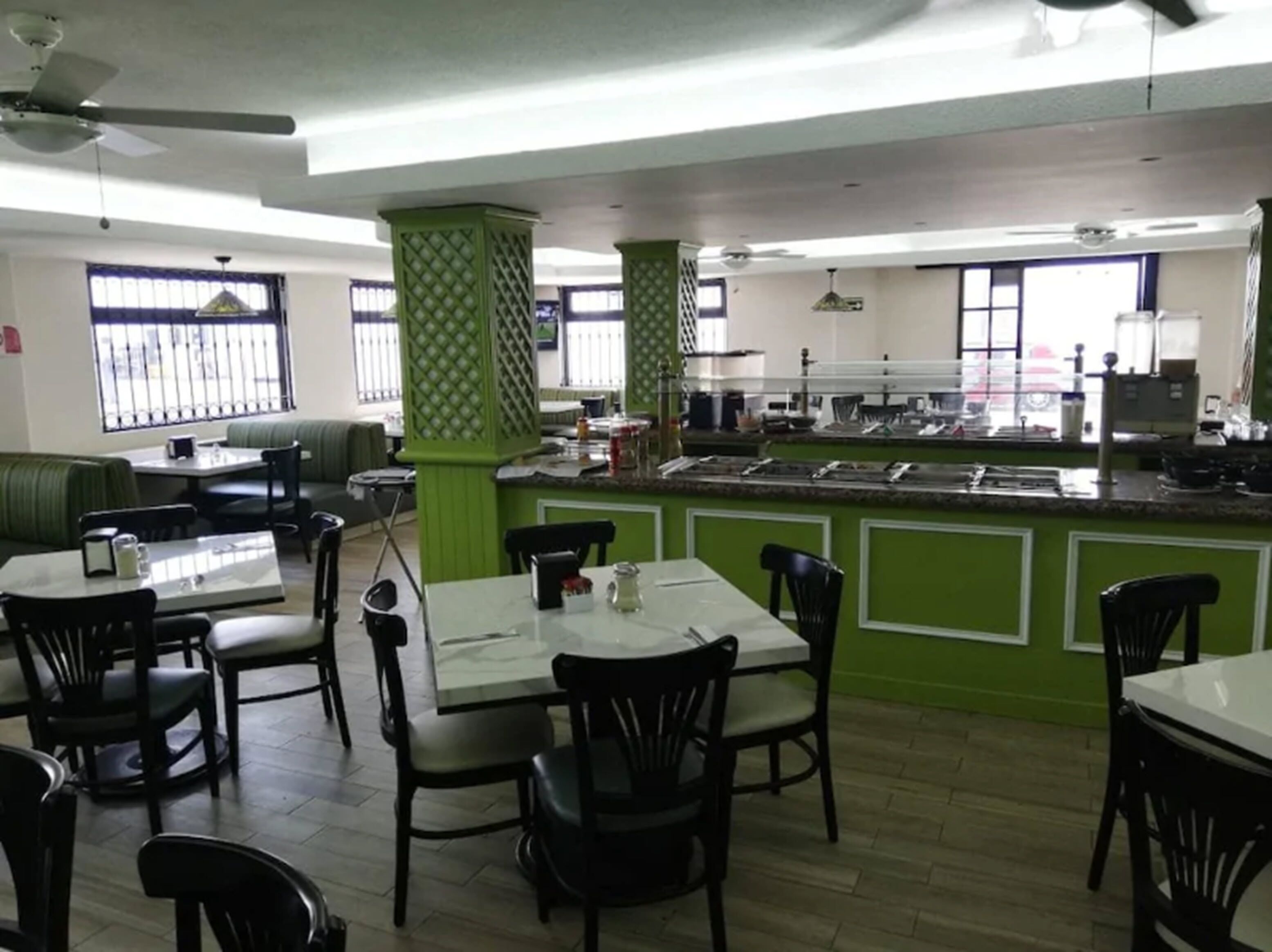 Un restaurante con paredes verdes, una barra con diferentes opciones de comida, y varias mesas y sillas.