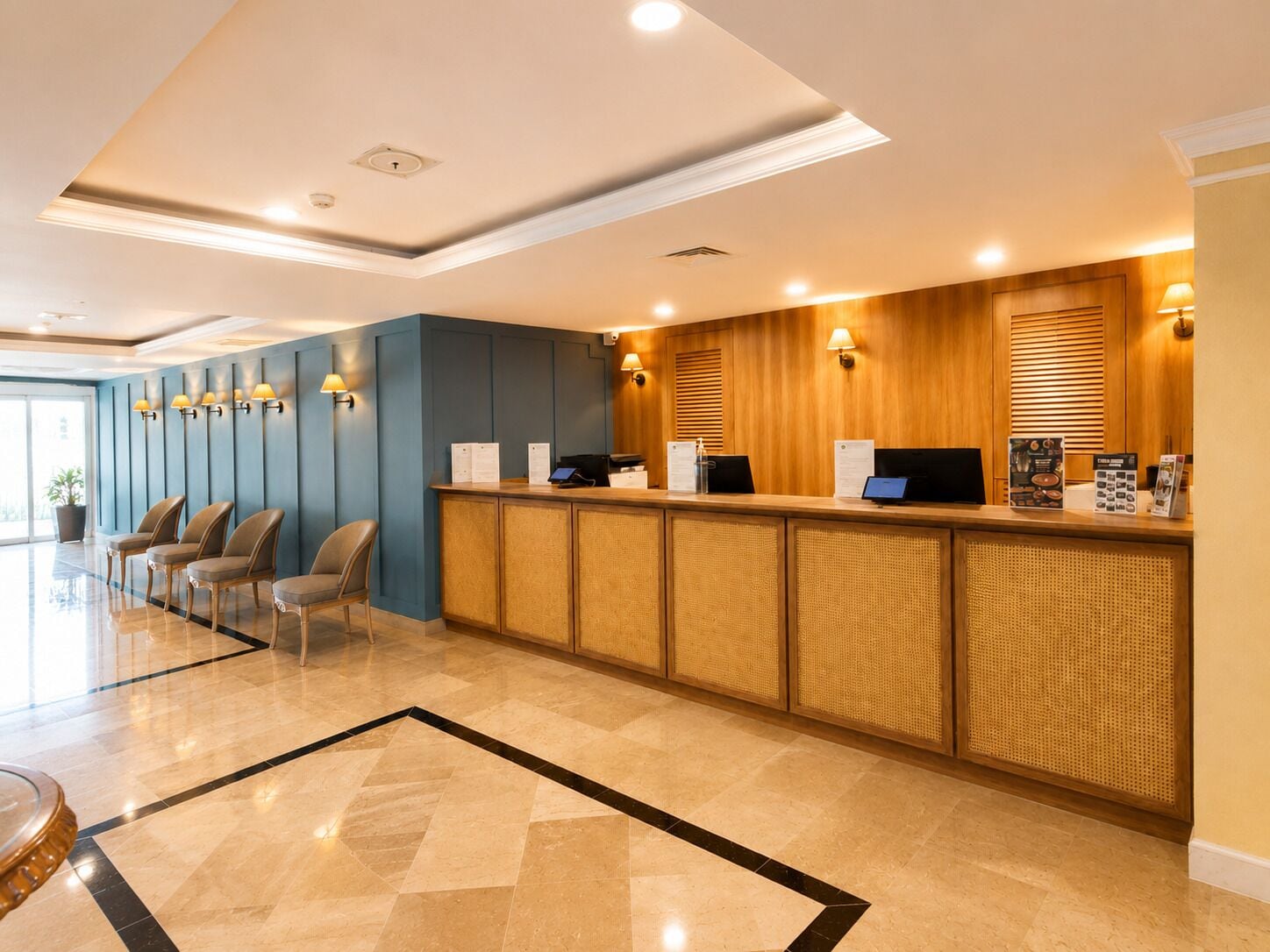 A hotel reception area with a reception desk, seating area, and a large window providing natural light.