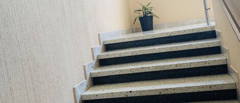 Eine Treppe aus Beton mit Metallgeländer, ein Blumentopf auf der Aussichtsplattform und ein kleines Fenster oben.