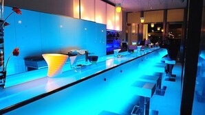 Un bar moderno con una barra alargada, iluminación azul ambiental y un gran jarrón decorativo.