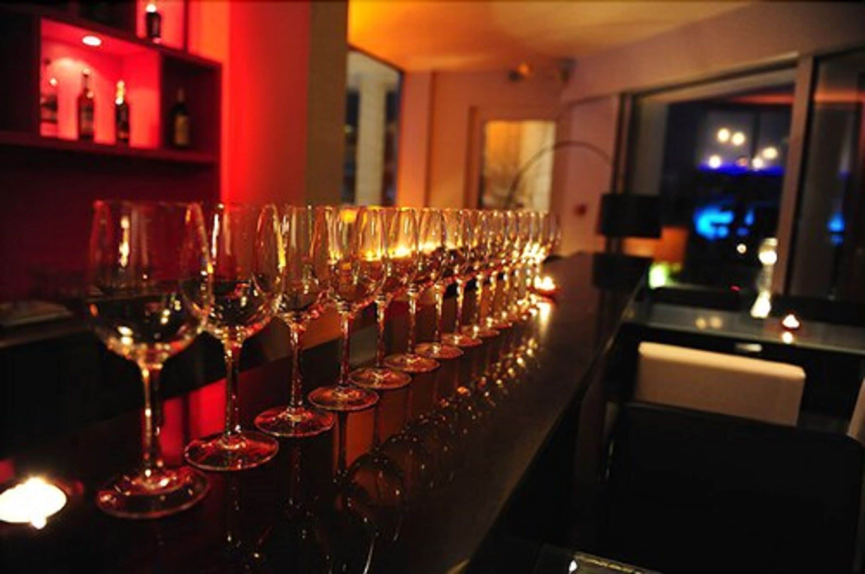 Una hilera de copas de vino vacías sobre una barra en un cuarto con poca luz y una iluminación ambiental roja.