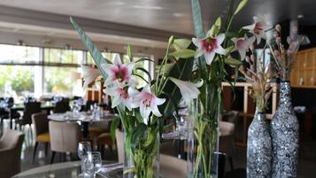 Interior de un restaurante con mesas preparadas para comer, destacando jarrones con flores y cristalería transparente.