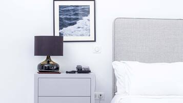 Un dormitorio con cama, mesita de noche con lámpara, teléfono y un cuadro en la pared.