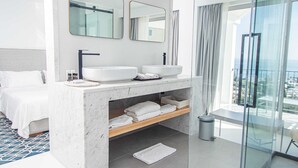 Un baño de hotel moderno con una ducha de vidrio amplia, un lavamanos blanco y un espejo grande.
