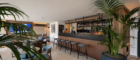 Zona de bar con taburetes, una barra con botellas y una planta grande en maceta.
