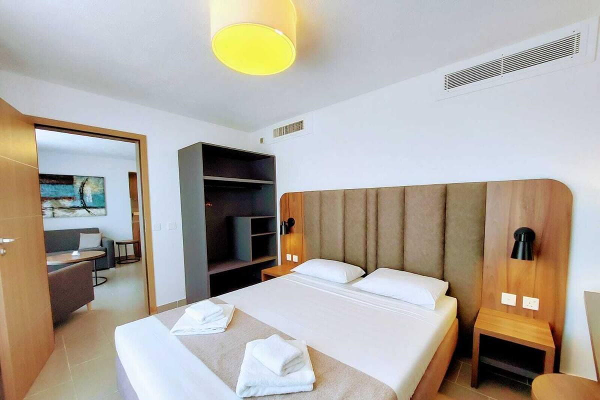 A modern hotel room with a large bed, a built-in wardrobe, a desk, and a seating area.