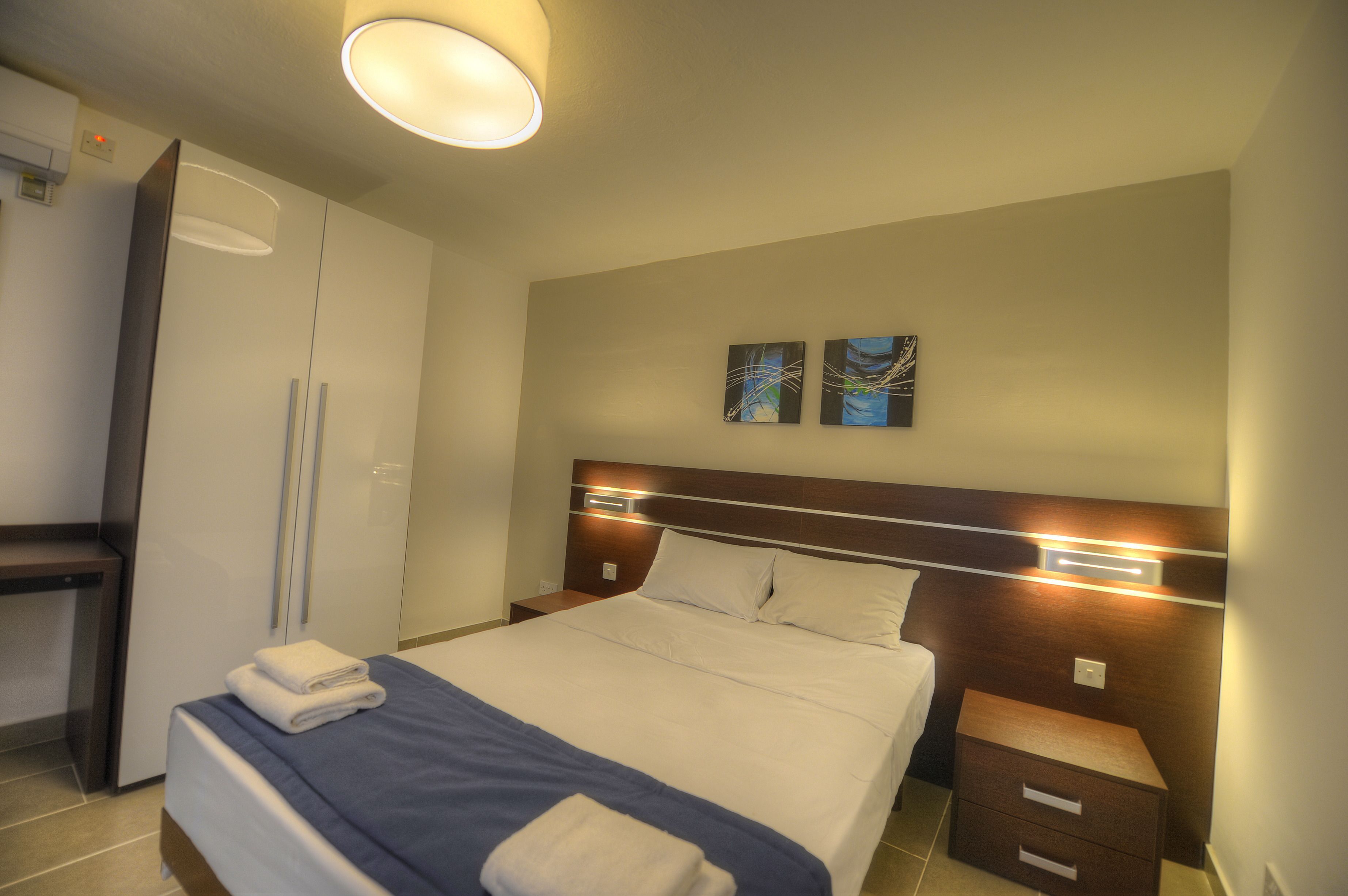 Ein Hotelzimmer mit Bett, Nachttischen, einem Kleiderschrank und Bildern an der Wand.