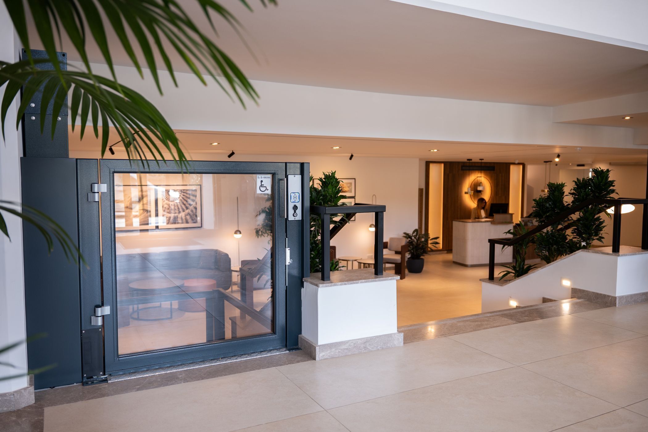 Un hall d’hôtel moderne comprenant un comptoir d’accueil, un espace salon et un escalier menant à l’étage supérieur.