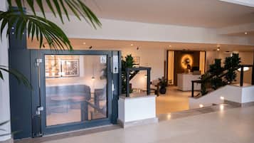 En modern hotellobby med en receptionsdisk, en sittgrupp och en trappa som leder upp till en våning ovanför.