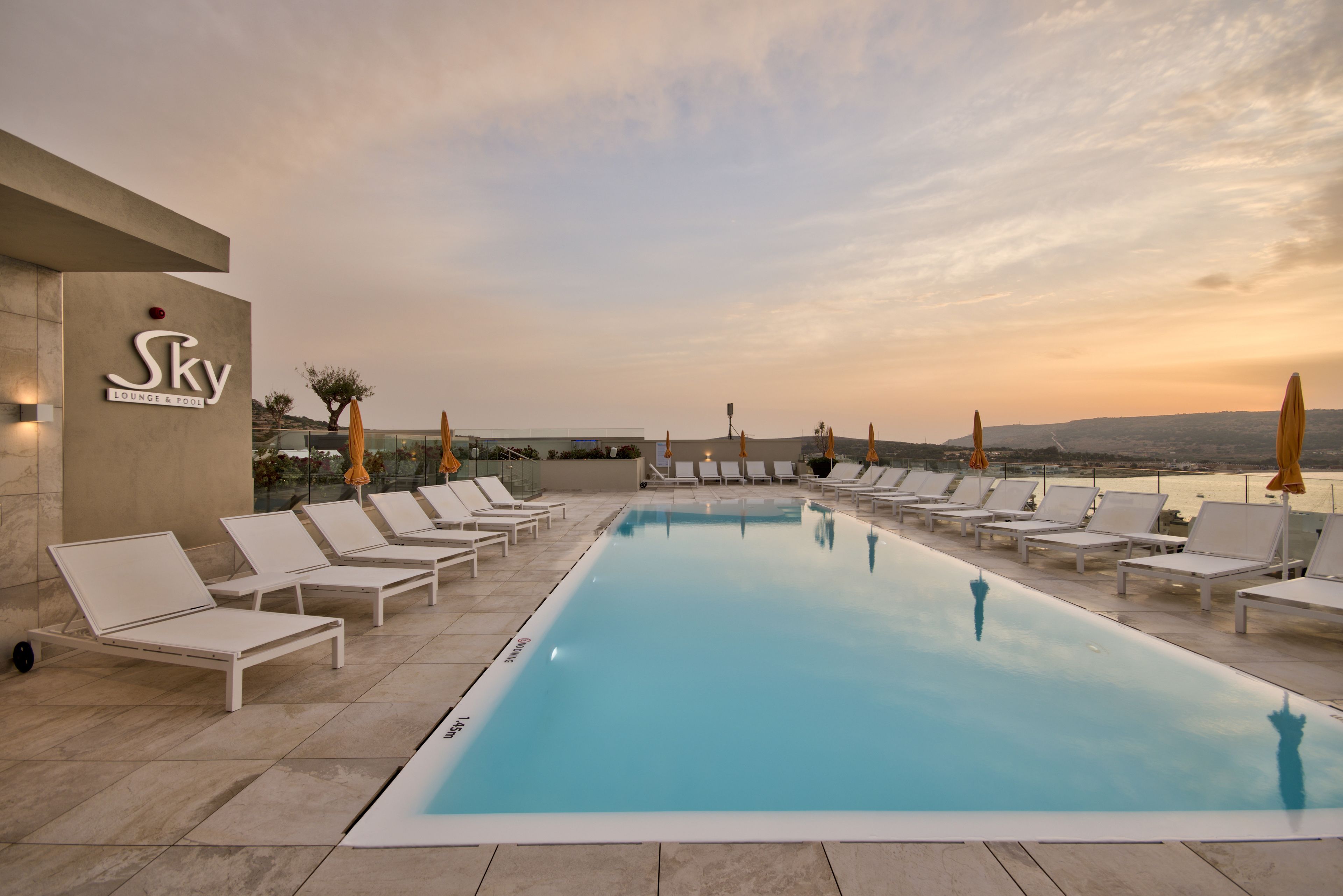 Ein Poolbereich mit Liegestühlen und Sonnenschirmen, wolkenloser Himmel und Blick auf die Landschaft.