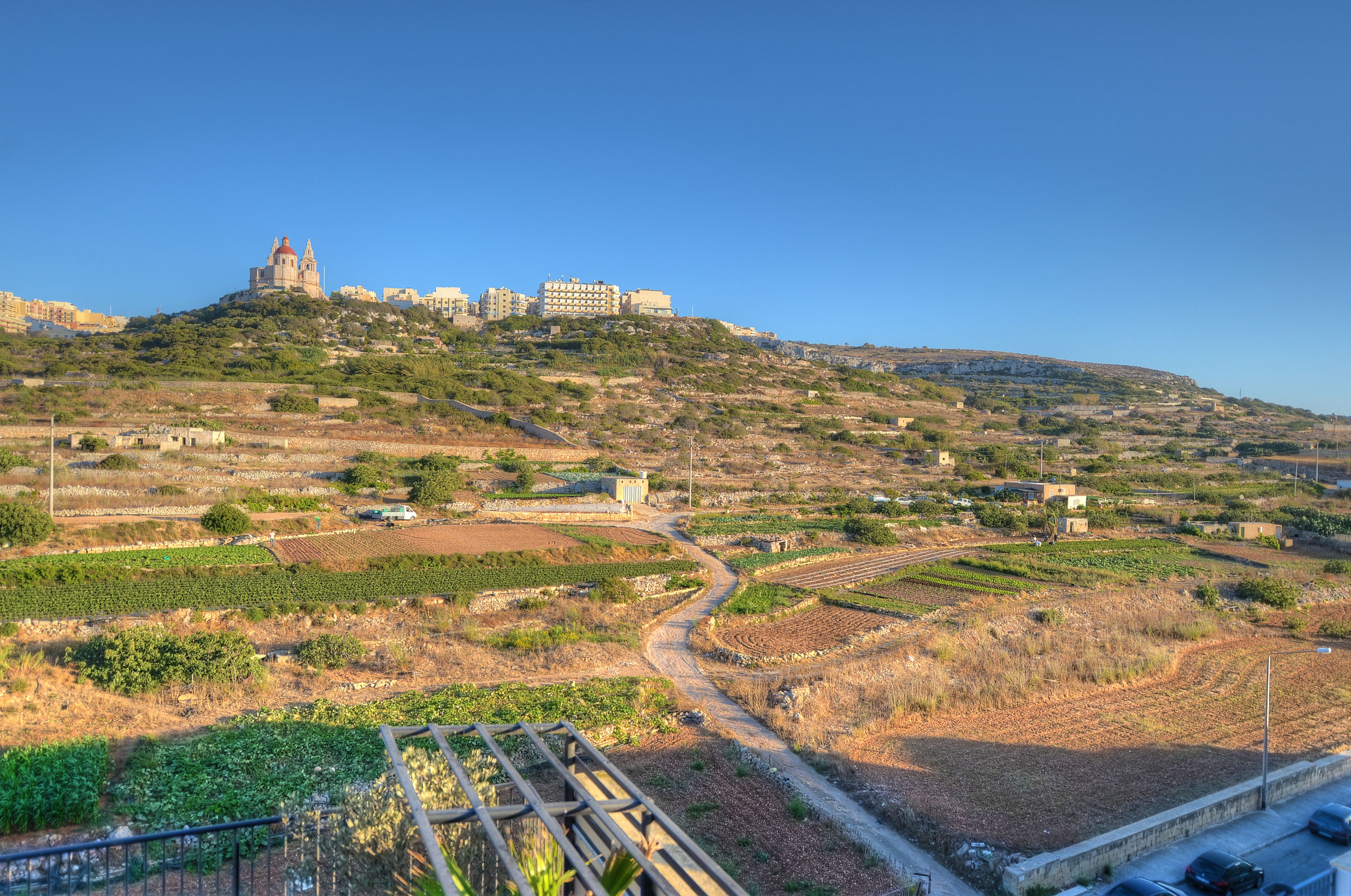 Un paysage côtier caractérisé par des champs en terrasses, une église imposante située sur une colline et une route qui serpente à travers le terrain.