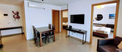 Una sala de estar moderna con un televisor de pantalla plana, un comedor con mesa y sillas de madera, y un sofá.
