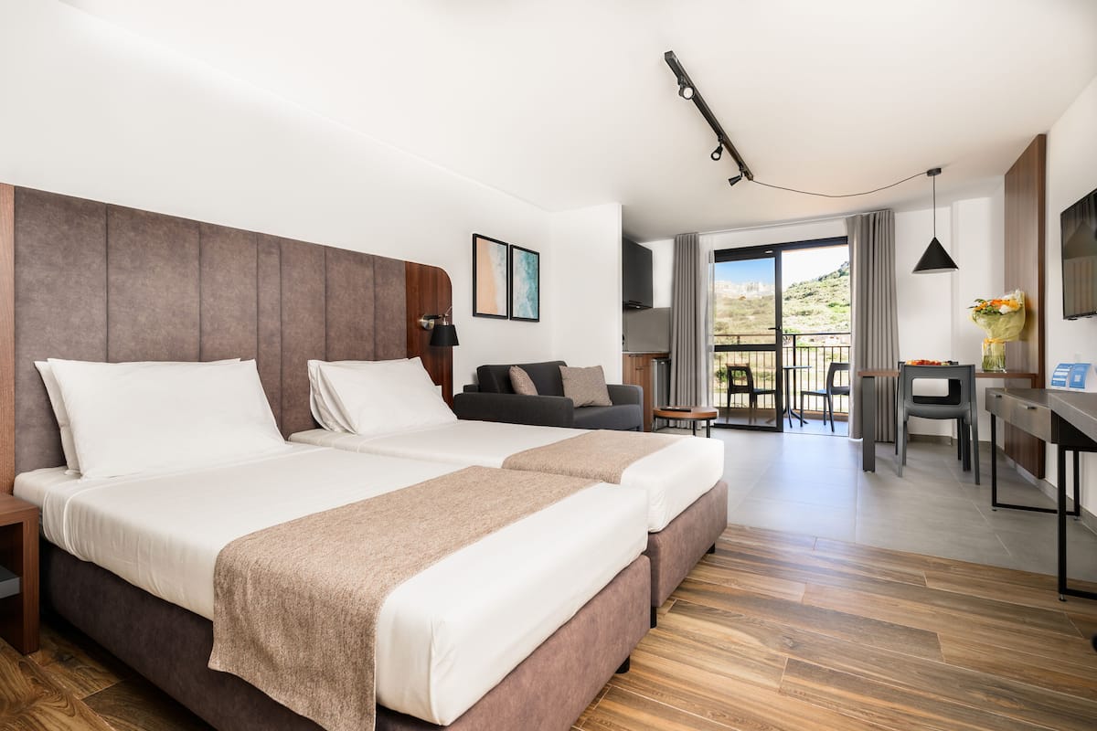 A modern hotel room with a large bed, a desk, and a balcony with a view.
