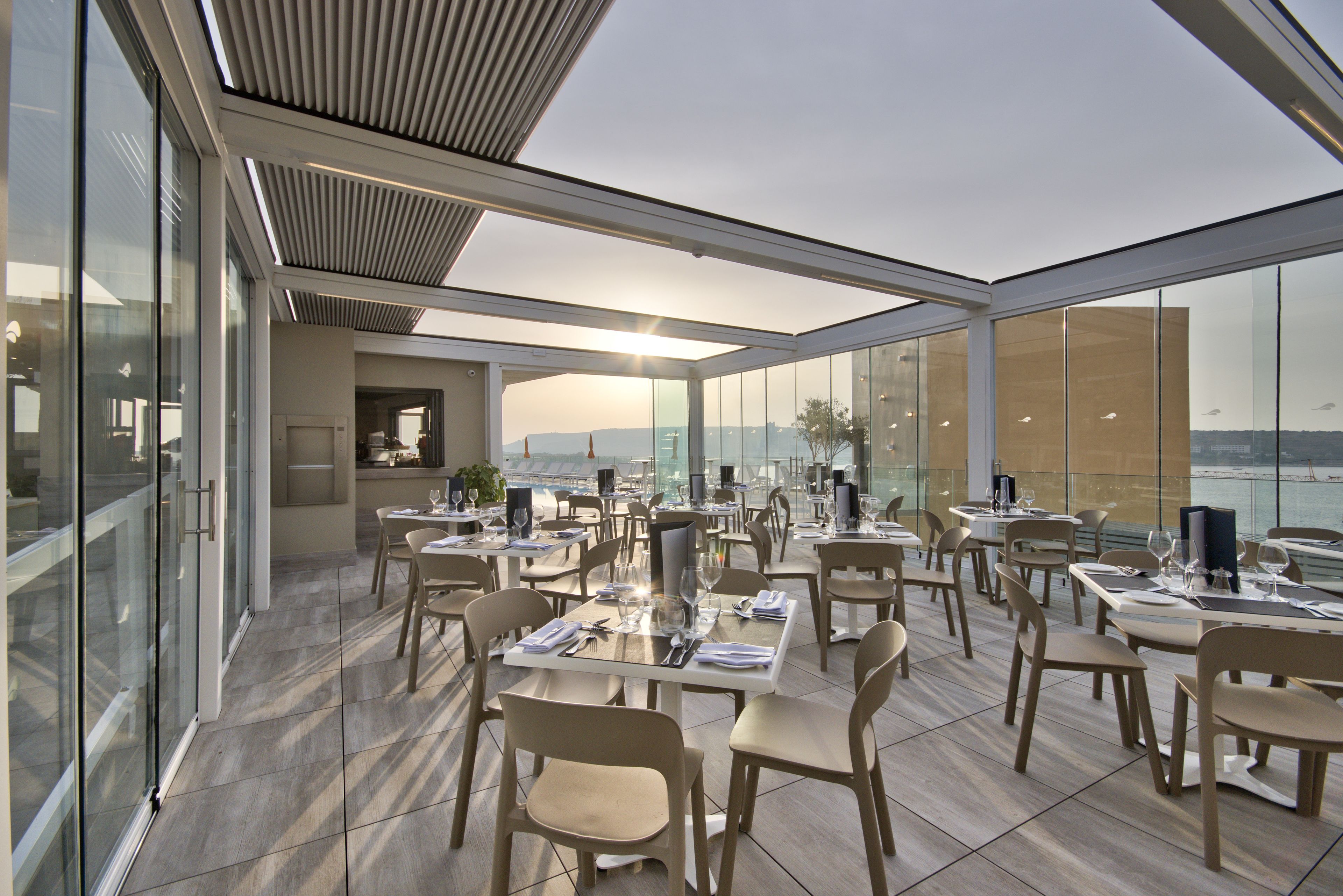 Un restaurante moderno con vistas panorámicas, que cuenta con un amplio comedor con numerosas mesas y sillas, y grandes ventanales que ofrecen una vista escénica.