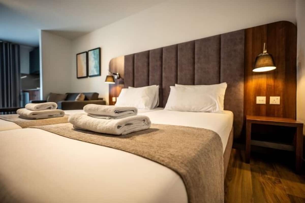 A hotel room with a large bed, a smaller bed, a wooden headboard, a bedside table, and a lamp.