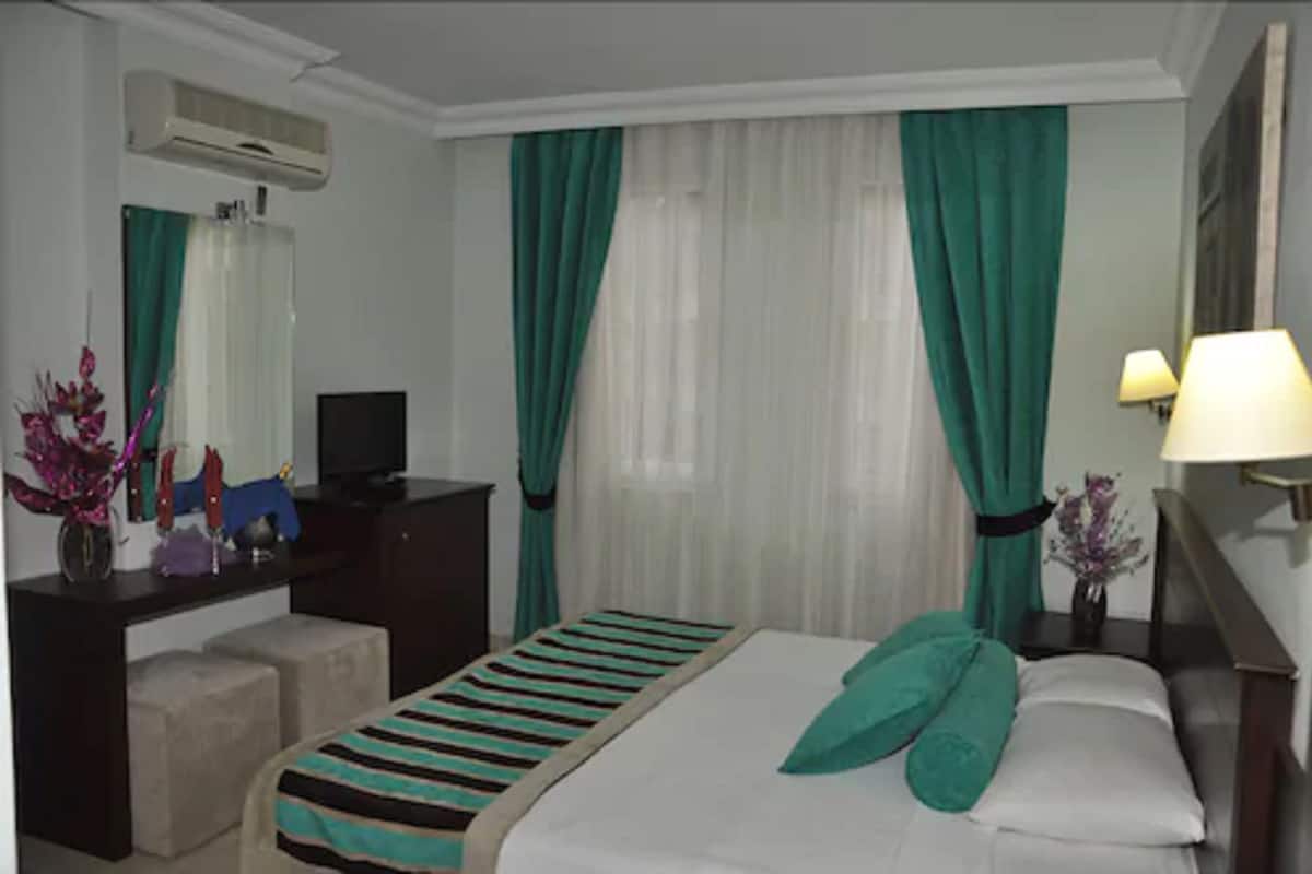 Une chambre d’hôtel avec un lit, un bureau, une chaise, une télévision et une lampe.