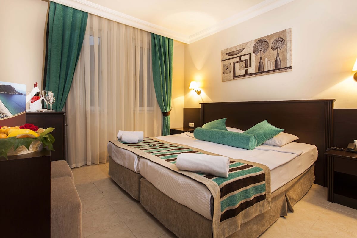 Une chambre d’hôtel avec un lit, une table de chevet, une lampe, un tableau et une fenêtre avec des rideaux.