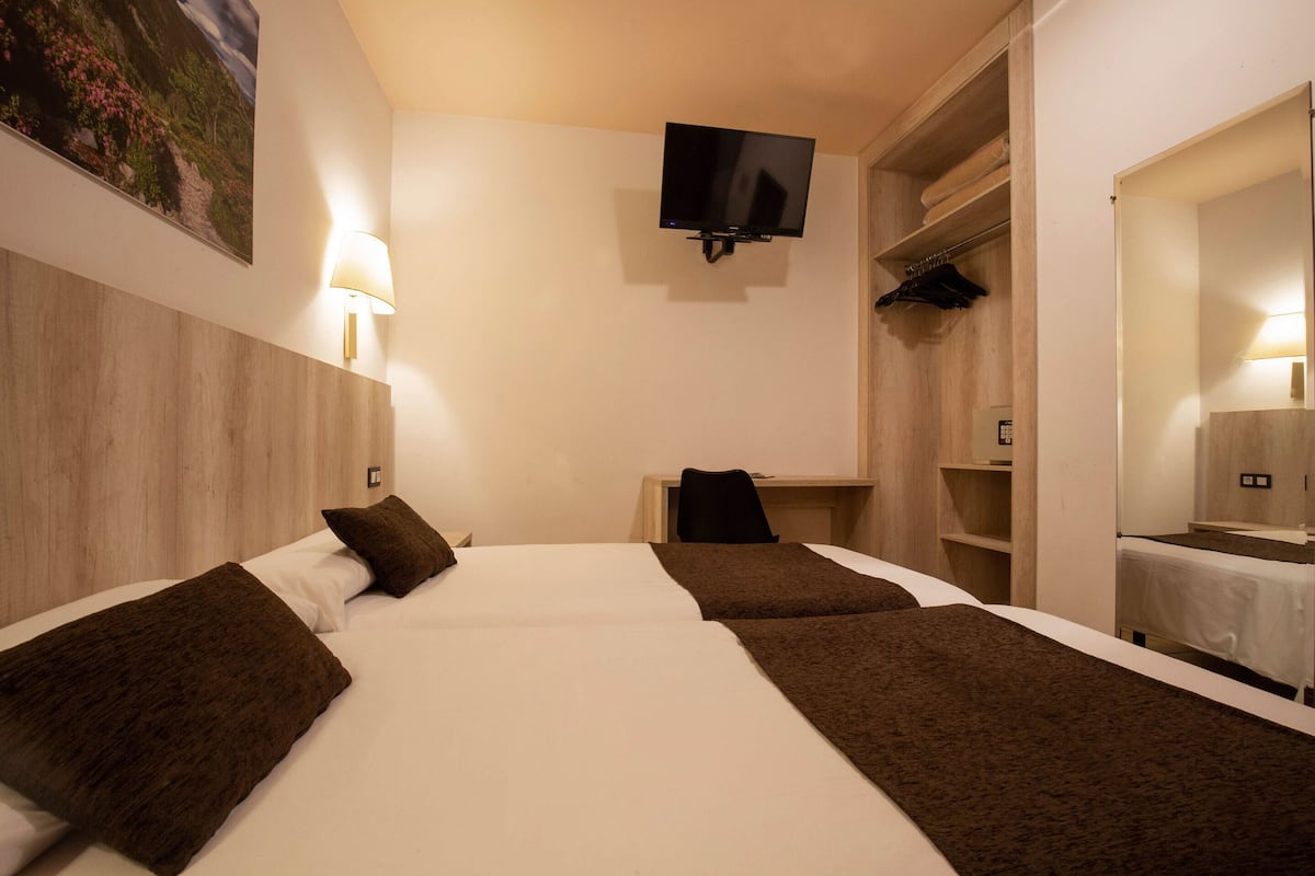 Hotellihuone, jossa on kaksi sänkyä, seinälle asennettu televisio, työpöytä ja erillinen vaatehuone.