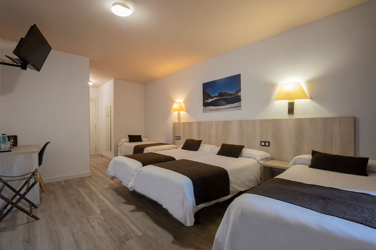 Hotellihuone, jossa on kolme sänkyä, työpöytä ja seinälle asennettu televisio.