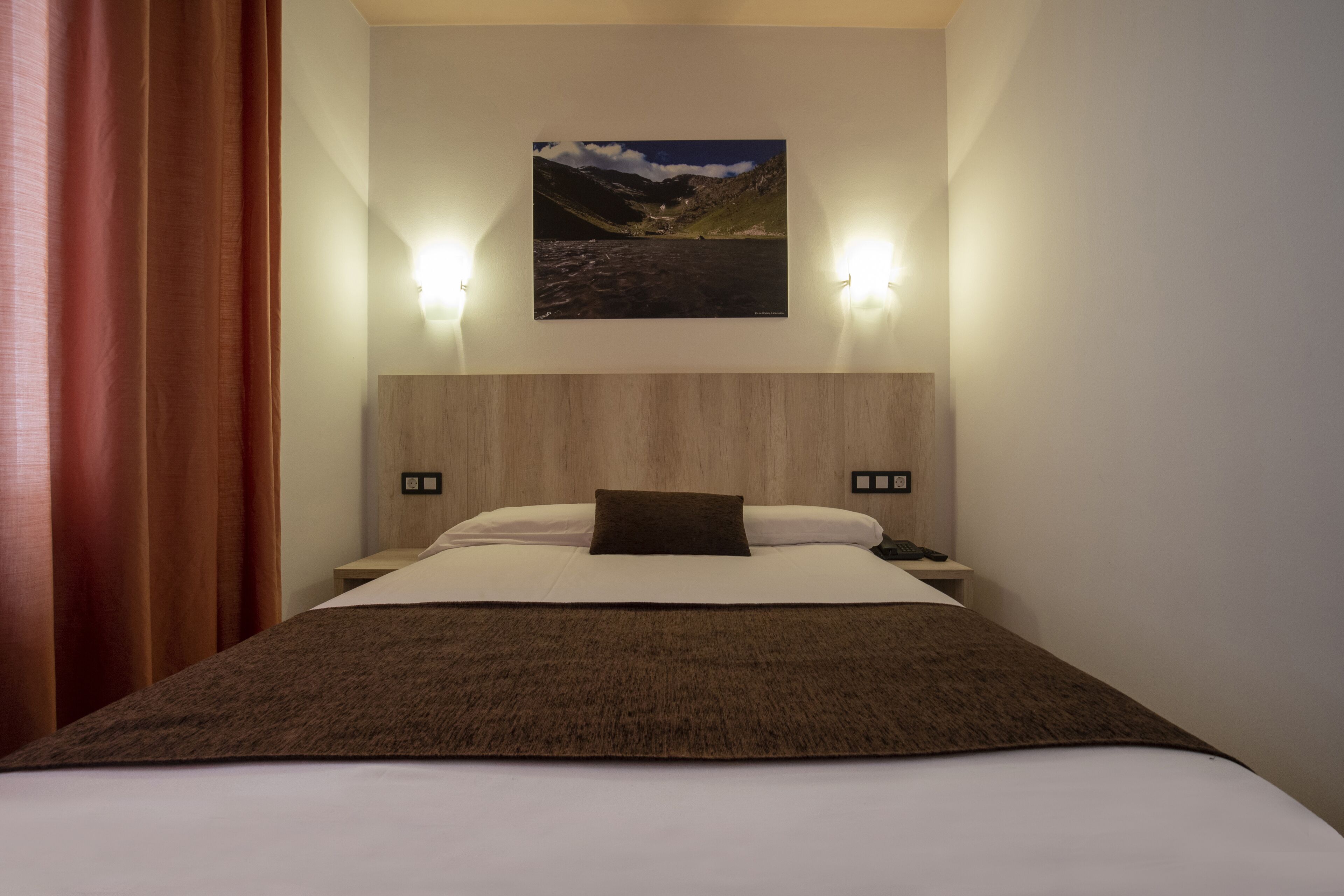 Una habitación de hotel con una cama, una mesita de noche, una lámpara y un cuadro colgado en la pared.