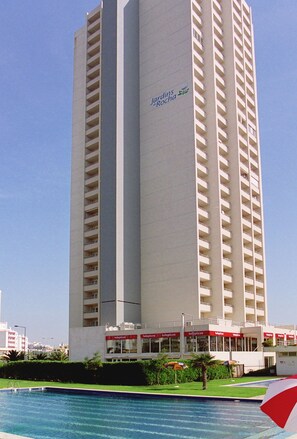 A tall hotel with a swimming pool in front. - Apartamentos Jardins da Rocha (Portimão)