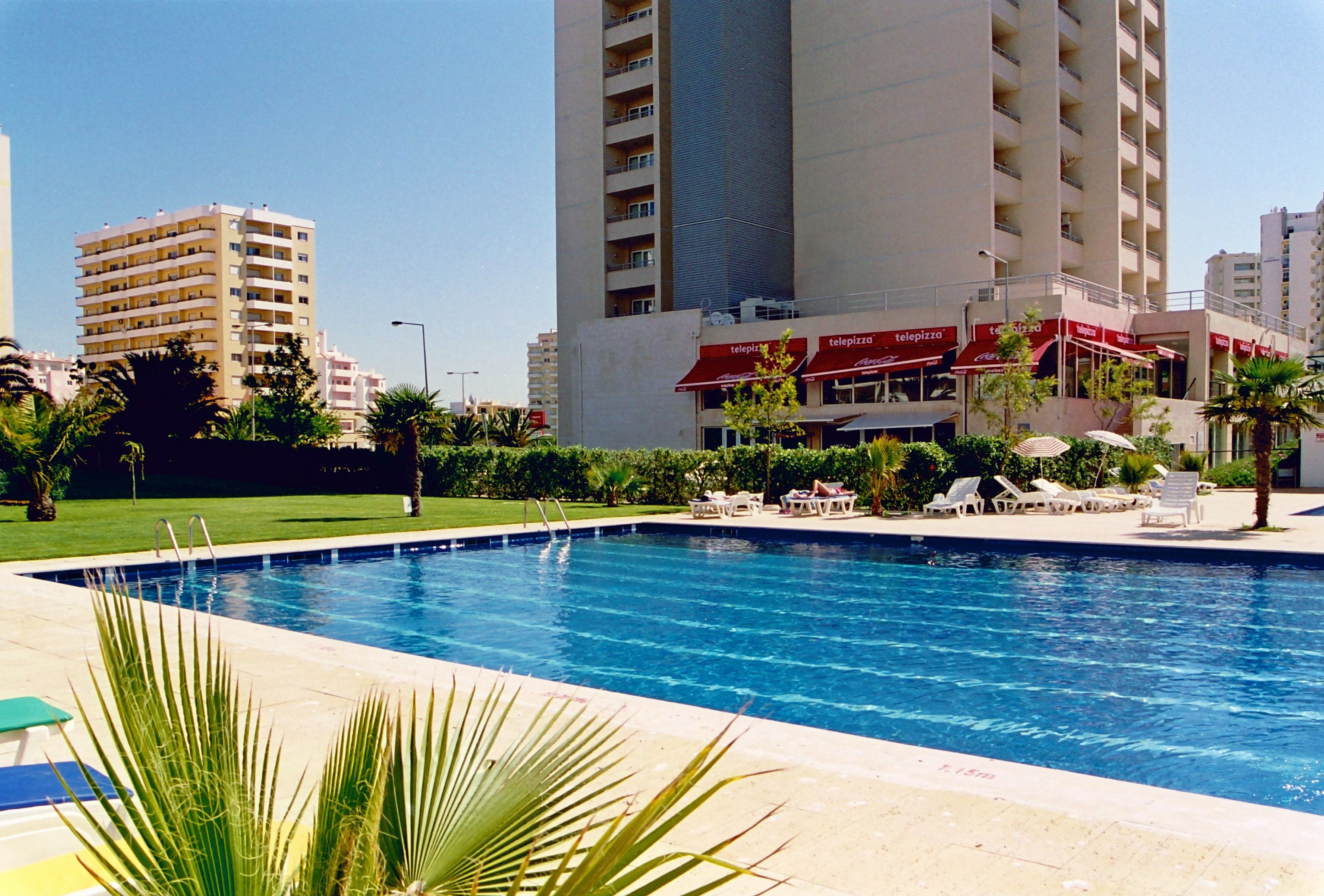 Una piscina con sillas de descanso y un restaurante con terraza.