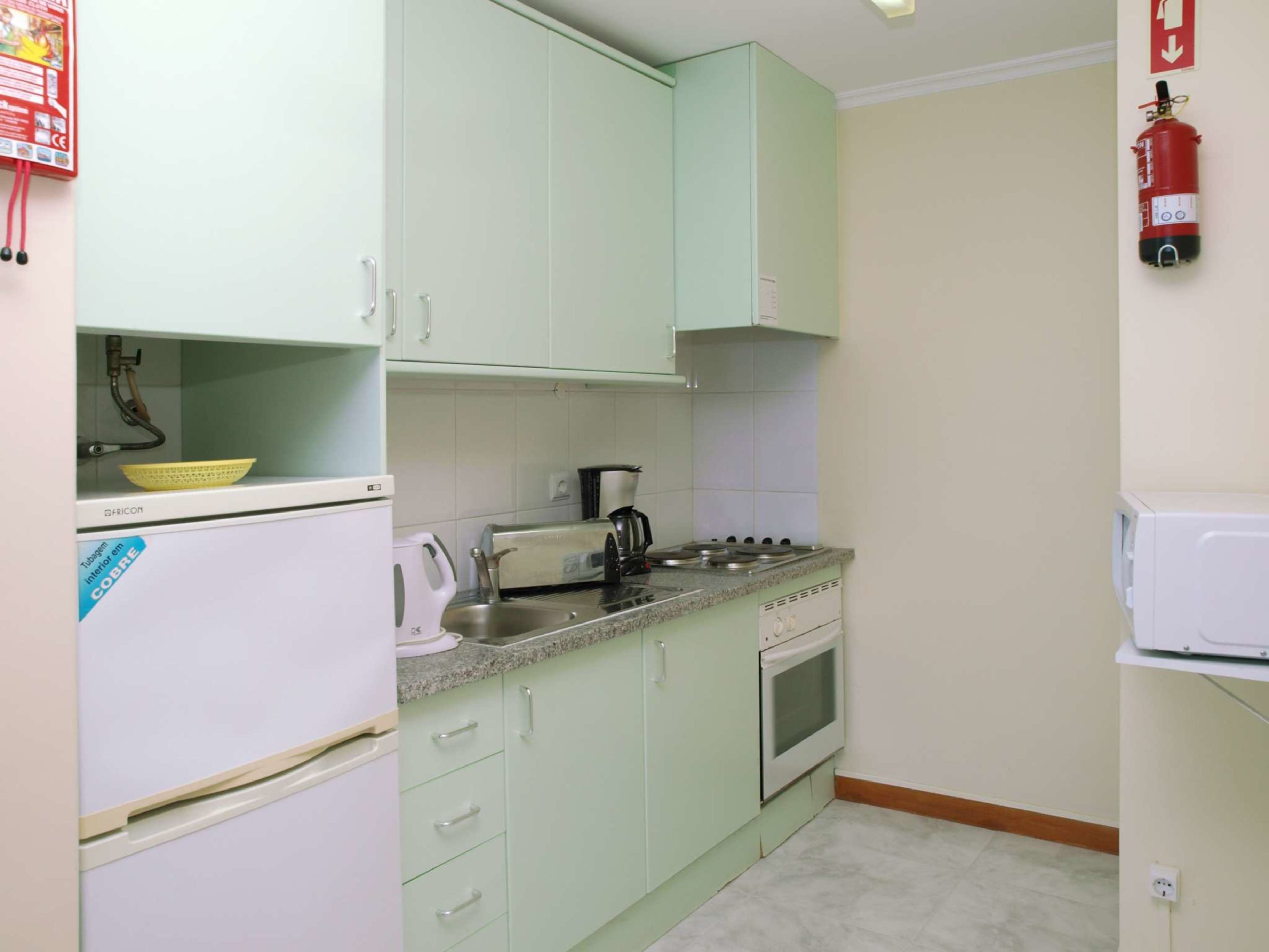 A kitchen with light green cabinets, a white refrigerator, a stove, and a sink.