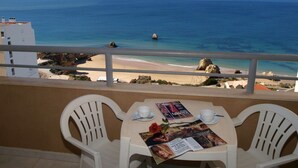 A balcony with a table set for two, overlooking a beach and the sea. - Apartamentos Jardins da Rocha (Portimão)