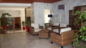 A lobby with wicker furniture, a potted plant, and a marble wall. - Apartamentos Jardins da Rocha (Portimão)