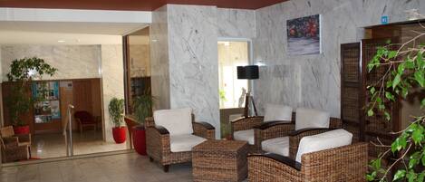 A lobby with wicker furniture, a potted plant, and a marble wall.