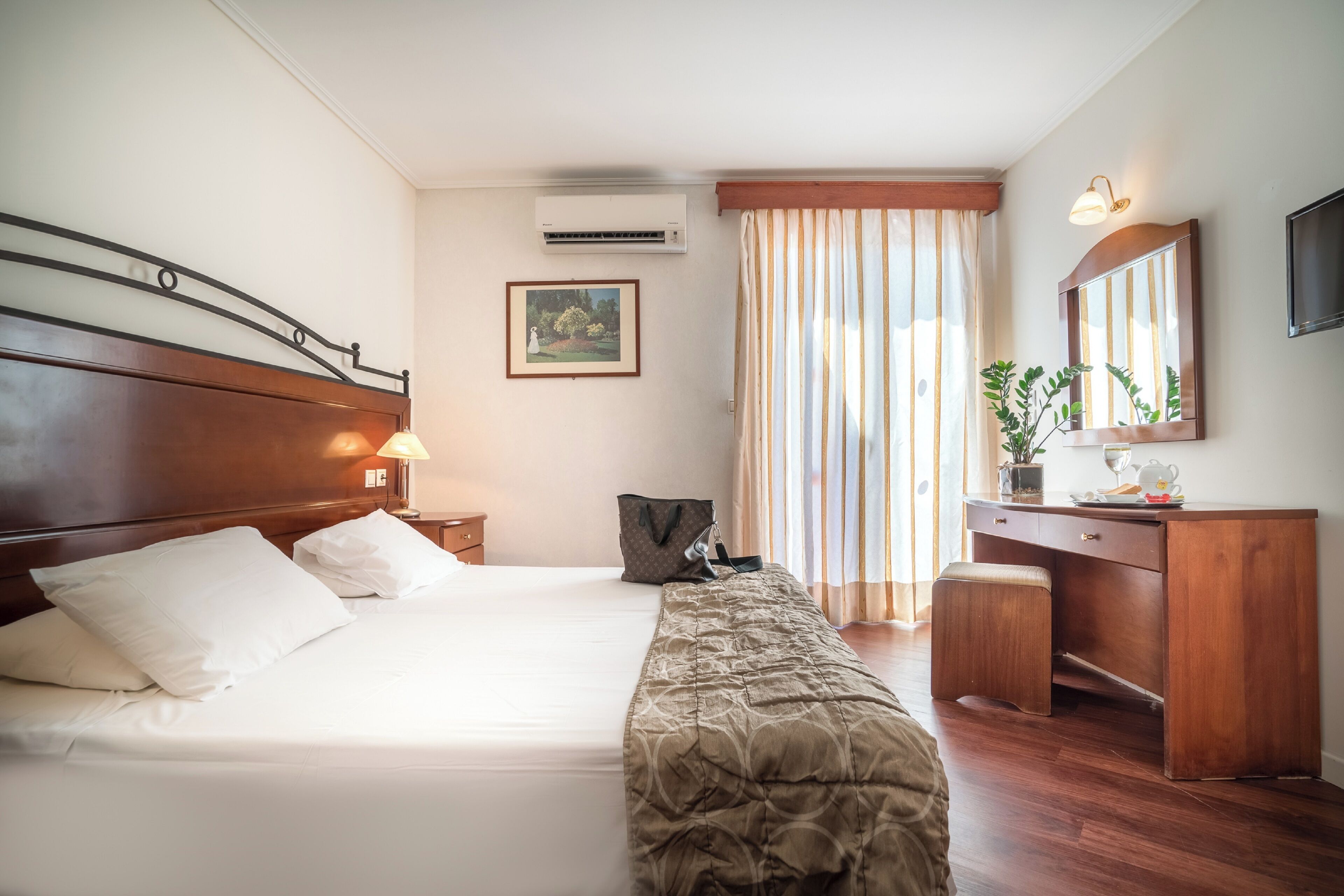 A hotel room with a wooden bed, a desk, a chair, a mirror, and a window with curtains.